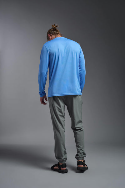 A blonde male model with a beard wearing the men's Oxymesh Long Sleeve Tech Tee in the color carolina blue on a gray background, made out of 100% polyester, showing the relaxed fit from a full body back view. This shirt is breathable, quick-drying, moisture-wicking, and made in the USA. #color_carolina-blue