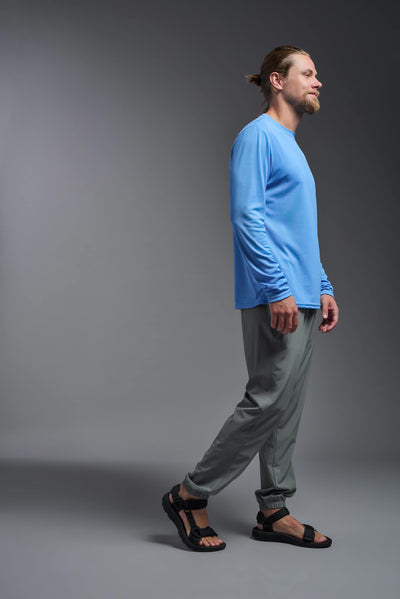 A blonde male model with a beard wearing the men's Oxymesh Long Sleeve Tech Tee in the color carolina blue on a gray background, made out of 100% polyester, showing the relaxed fit from a full body side view. This shirt is breathable, quick-drying, moisture-wicking, and made in the USA. #color_carolina-blue