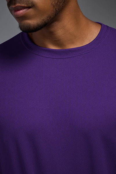 An African American male model with a beard wearing the men's Oxymesh Long Sleeve Tech Tee in the color dark purple, made out of 100% polyester, showing the relaxed fit from a closeup collar view. This shirt is breathable, quick-drying, moisture-wicking, and made in the USA. #color_dark-purple