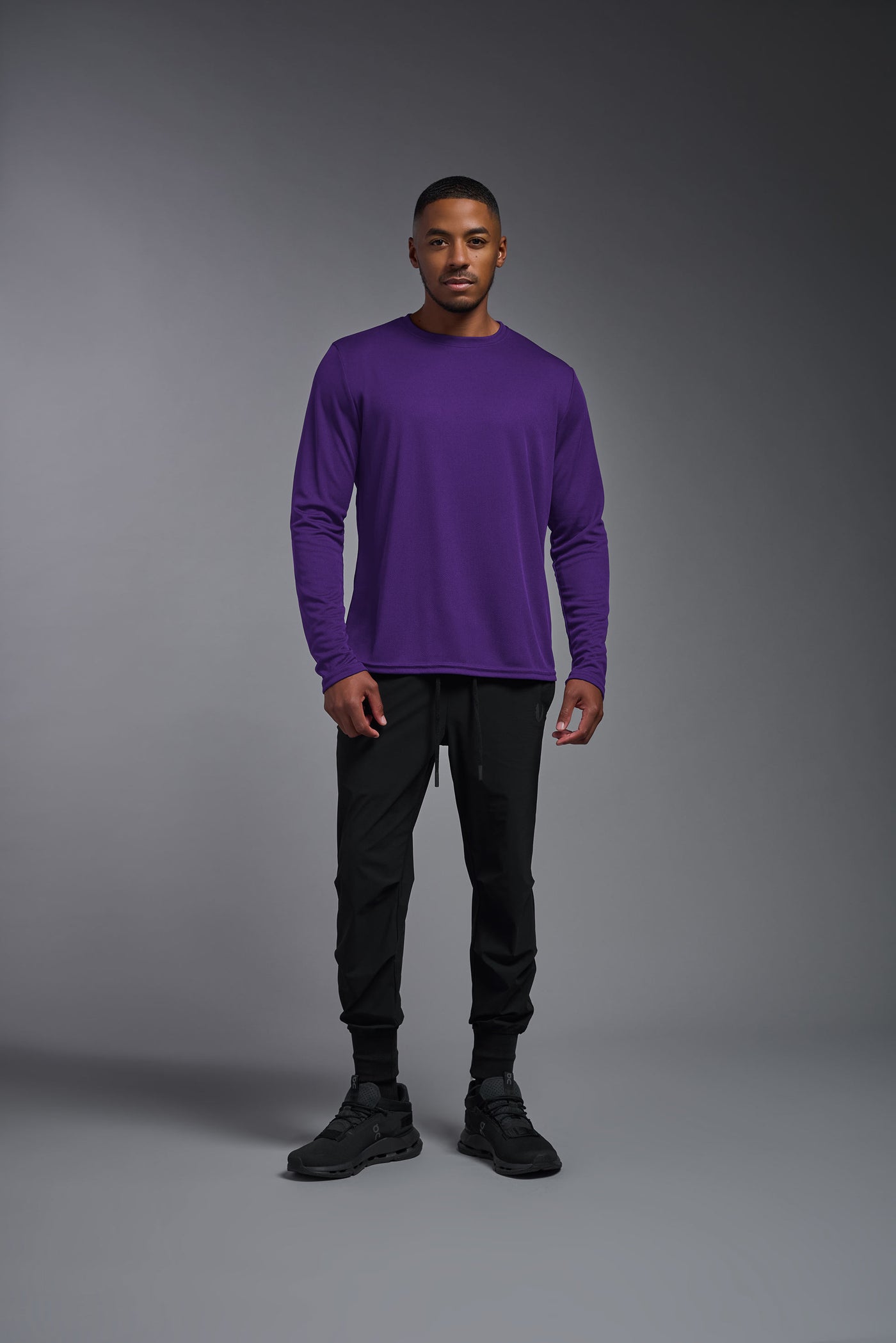 An African American male model with a beard wearing the men's Oxymesh Long Sleeve Tech Tee in the color dark purple, made out of 100% polyester, showing the relaxed fit from a front view. This shirt is breathable, quick-drying, moisture-wicking, and made in the USA. #color_dark-purple