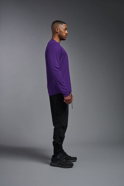 An African American male model with a beard wearing the men's Oxymesh Long Sleeve Tech Tee in the color dark purple, made out of 100% polyester, showing the relaxed fit from a full body side view. This shirt is breathable, quick-drying, moisture-wicking, and made in the USA. #color_dark-purple