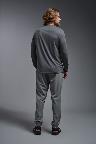 A blonde American male model with a beard wearing the men's Oxymesh Long Sleeve Tech Tee in the color graphite gray, made out of 100% polyester, showing the relaxed fit from a full body back view. This shirt is breathable, quick-drying, moisture-wicking, and made in the USA. #color_graphite-gray