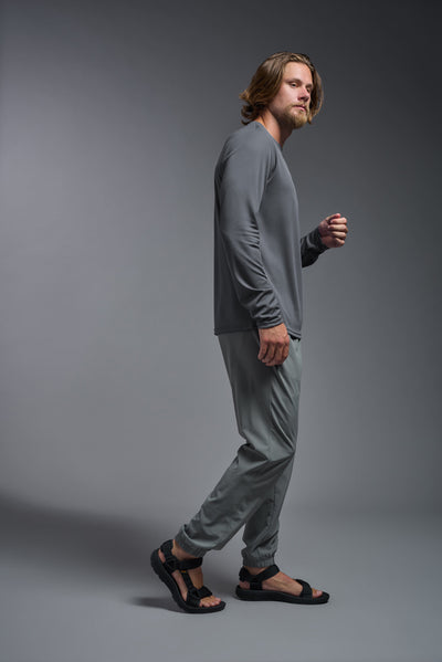 A blonde American male model with a beard wearing the men's Oxymesh Long Sleeve Tech Tee in the color graphite gray, made out of 100% polyester, showing the relaxed fit from a full body side view. This shirt is breathable, quick-drying, moisture-wicking, and made in the USA. #color_graphite-gray