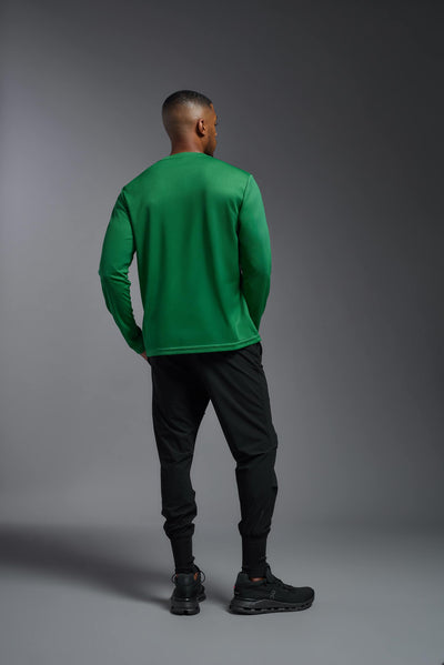 An African American male model with a beard wearing the men's Oxymesh Long Sleeve Tech Tee in the color kelly green on a gray background, made out of 100% polyester, showing the relaxed fit from a full body back view. This shirt is breathable, quick-drying, moisture-wicking, and made in the USA. #color_kelly-green