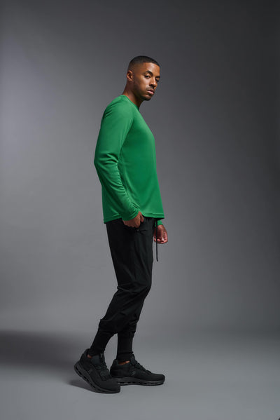 An African American male model with a beard wearing the men's Oxymesh Long Sleeve Tech Tee in the color kelly green on a gray background, made out of 100% polyester, showing the relaxed fit from a full body side view. This shirt is breathable, quick-drying, moisture-wicking, and made in the USA. #color_kelly-green