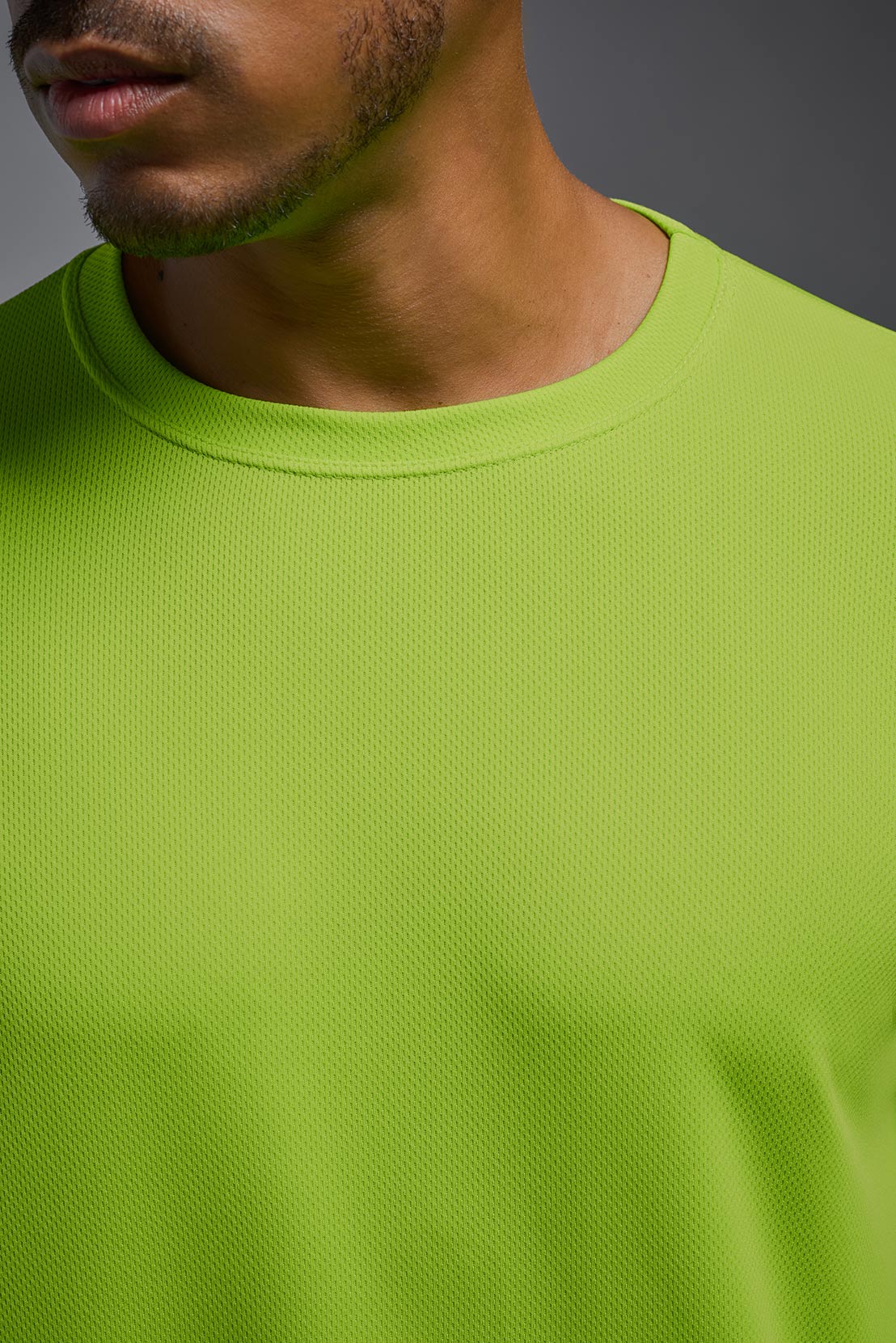 An African American male model with a beard wearing the men's Oxymesh Long Sleeve Tech Tee in the color key lime on a gray background, made out of 100% polyester, showing the relaxed fit from a closeup collar front view. This shirt is breathable, quick-drying, moisture-wicking, and made in the USA. #color_key-lime