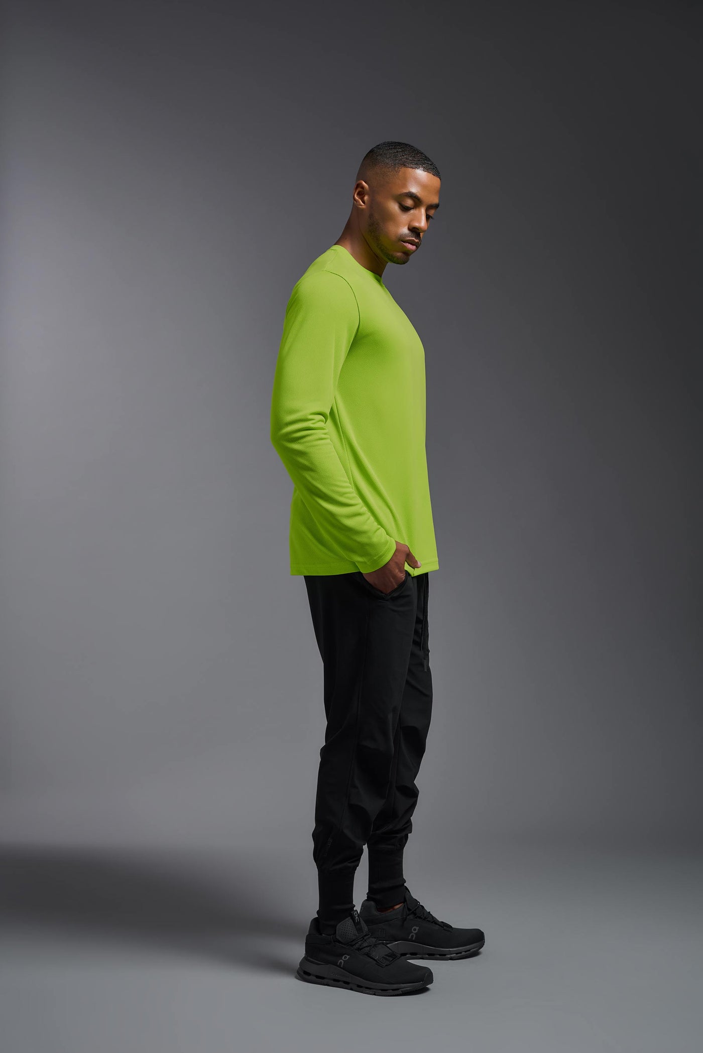 An African American male model with a beard wearing the men's Oxymesh Long Sleeve Tech Tee in the color key lime on a gray background, made out of 100% polyester, showing the relaxed fit from a full body side view. This shirt is breathable, quick-drying, moisture-wicking, and made in the USA. #color_key-lime