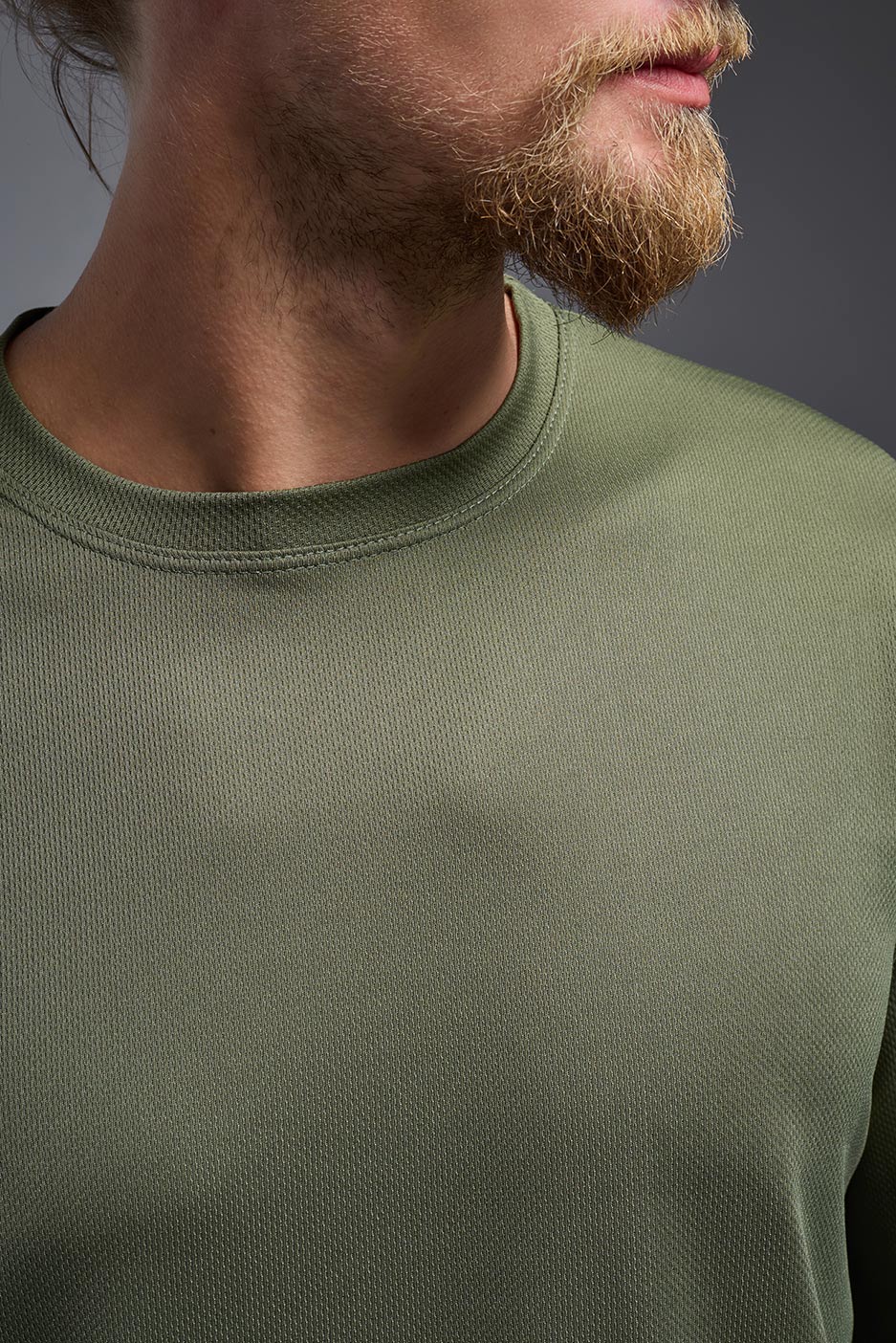 A blonde Caucasian male model with a beard wearing the men's Oxymesh Long Sleeve Tech Tee in the color military green on a gray background, made out of 100% polyester, showing the relaxed fit from a front collar view. This shirt is breathable, quick-drying, moisture-wicking, and made in the USA. #color_military-green