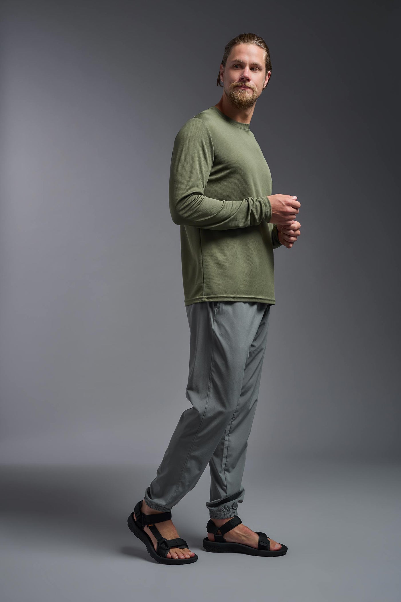 A blonde Caucasian male model with a beard wearing the men's Oxymesh Long Sleeve Tech Tee in the color military green on a gray background, made out of 100% polyester, showing the relaxed fit from a side view. This shirt is breathable, quick-drying, moisture-wicking, and made in the USA. #color_military-green