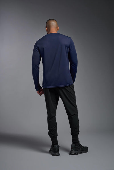 An African American male model with a beard wearing the men's Oxymesh Long Sleeve Tech Tee in the color navy on a gray background, made out of 100% polyester, showing the relaxed fit from a full body back view. This shirt is breathable, quick-drying, moisture-wicking, and made in the USA. #color_navy