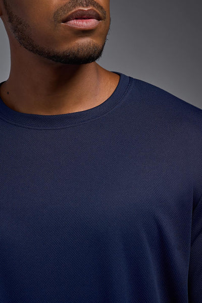 An African American male model with a beard wearing the men's Oxymesh Long Sleeve Tech Tee in the color navy on a gray background, made out of 100% polyester, showing the relaxed fit from a closeup collar front view. This shirt is breathable, quick-drying, moisture-wicking, and made in the USA. #color_navy