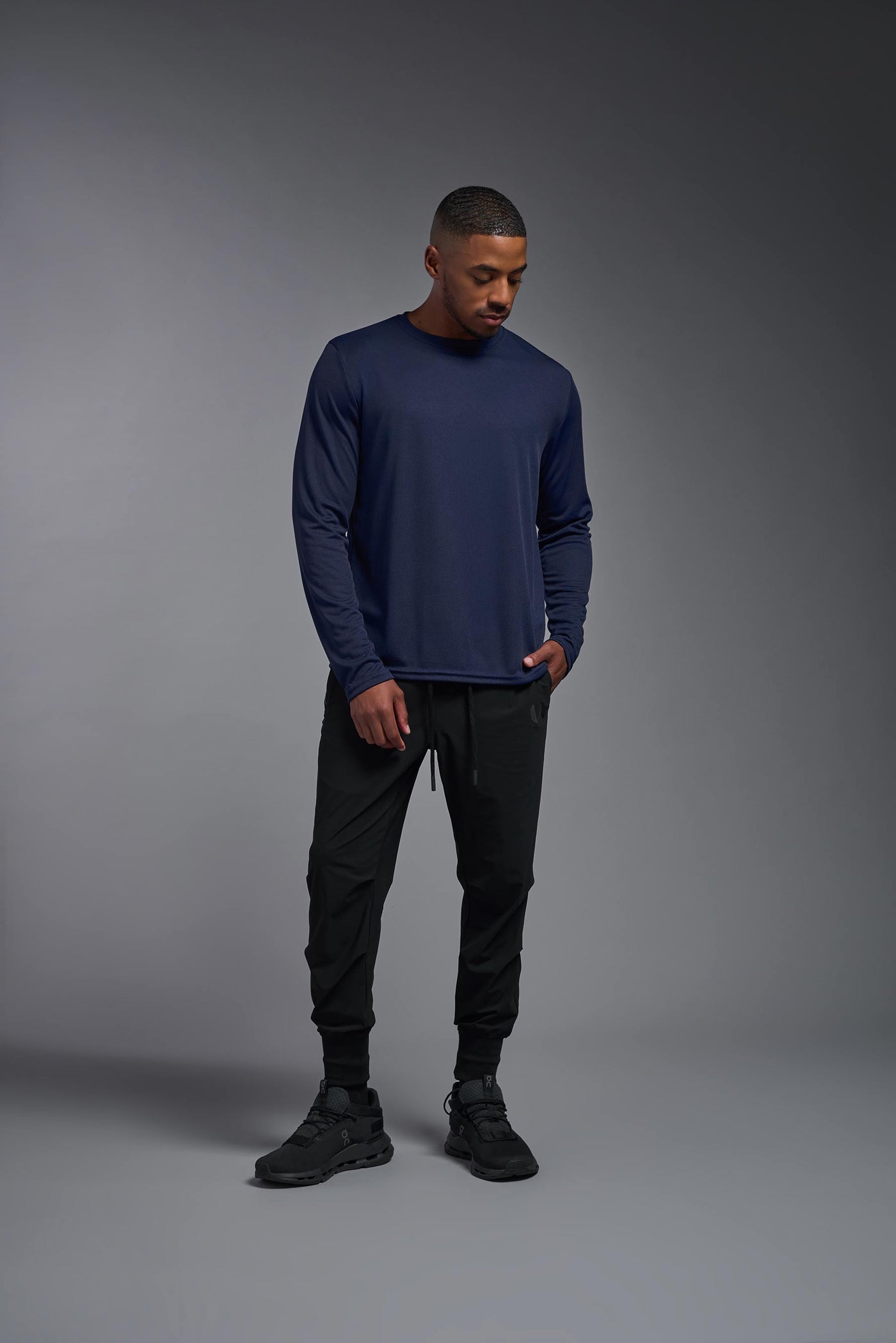 An African American male model with a beard wearing the men's Oxymesh Long Sleeve Tech Tee in the color navy on a gray background, made out of 100% polyester, showing the relaxed fit from a full body front view. This shirt is breathable, quick-drying, moisture-wicking, and made in the USA. #color_navy