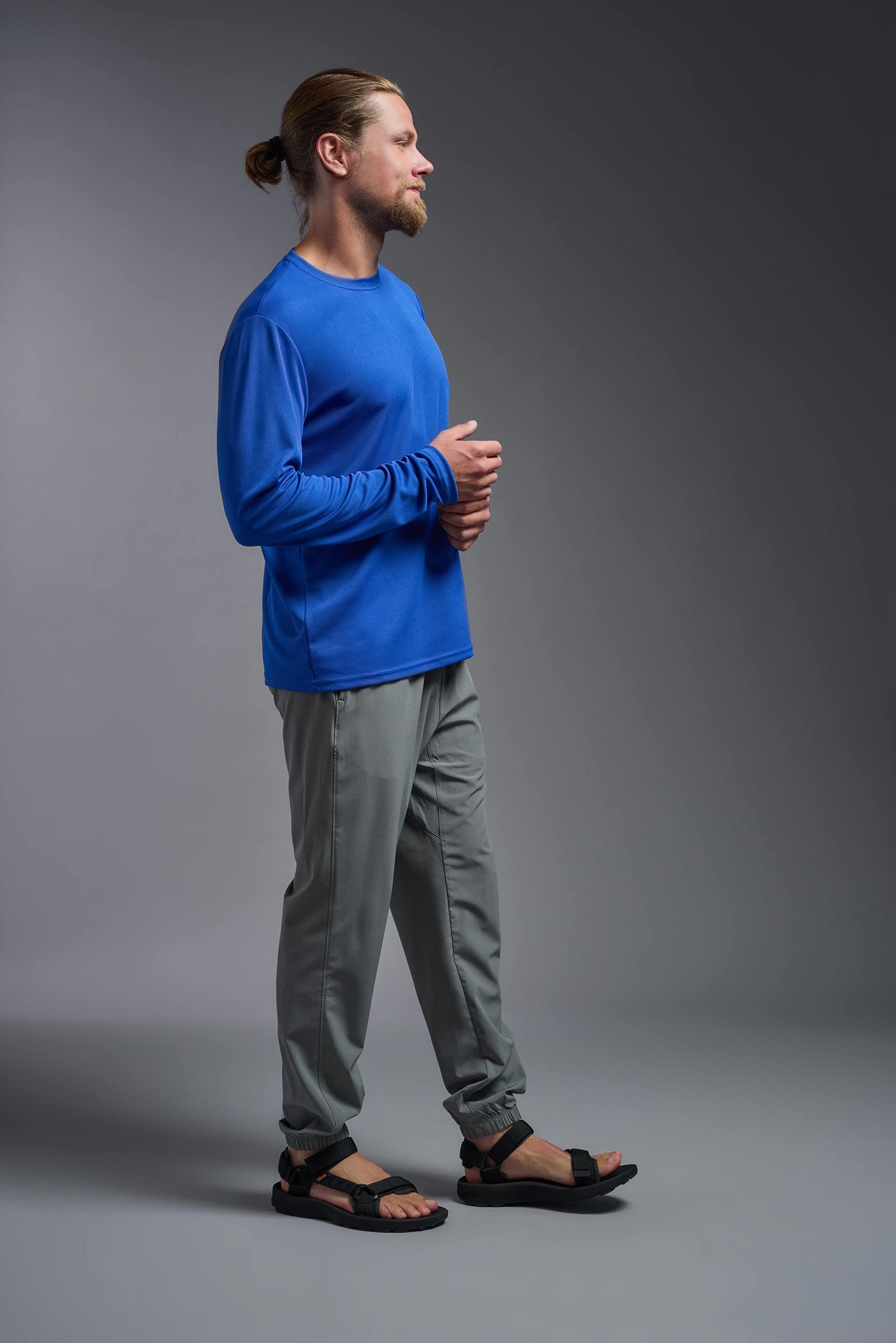 A blonde male model with a beard wearing the men's Oxymesh Long Sleeve Tech Tee in the color royal blue on a gray background, made out of 100% polyester, showing the relaxed fit from a full body side view. This shirt is breathable, quick-drying, moisture-wicking, and made in the USA. #color_royal-blue