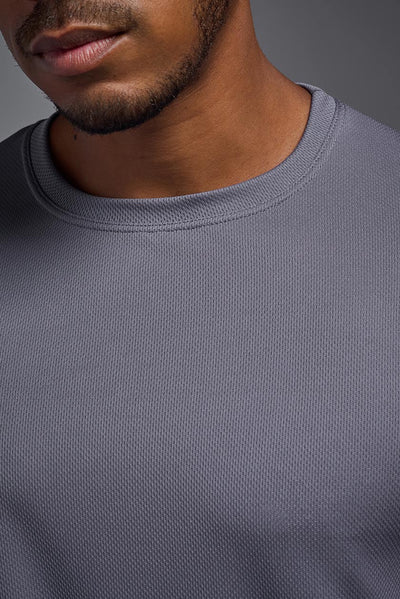 An African American male model with a beard wearing the men's Oxymesh Long Sleeve Tech Tee in the color steel gray on a gray background, made out of 100% polyester, showing the relaxed fit from a collar closeup view. This shirt is breathable, quick-drying, moisture-wicking, and made in the USA. #color_steel-gray