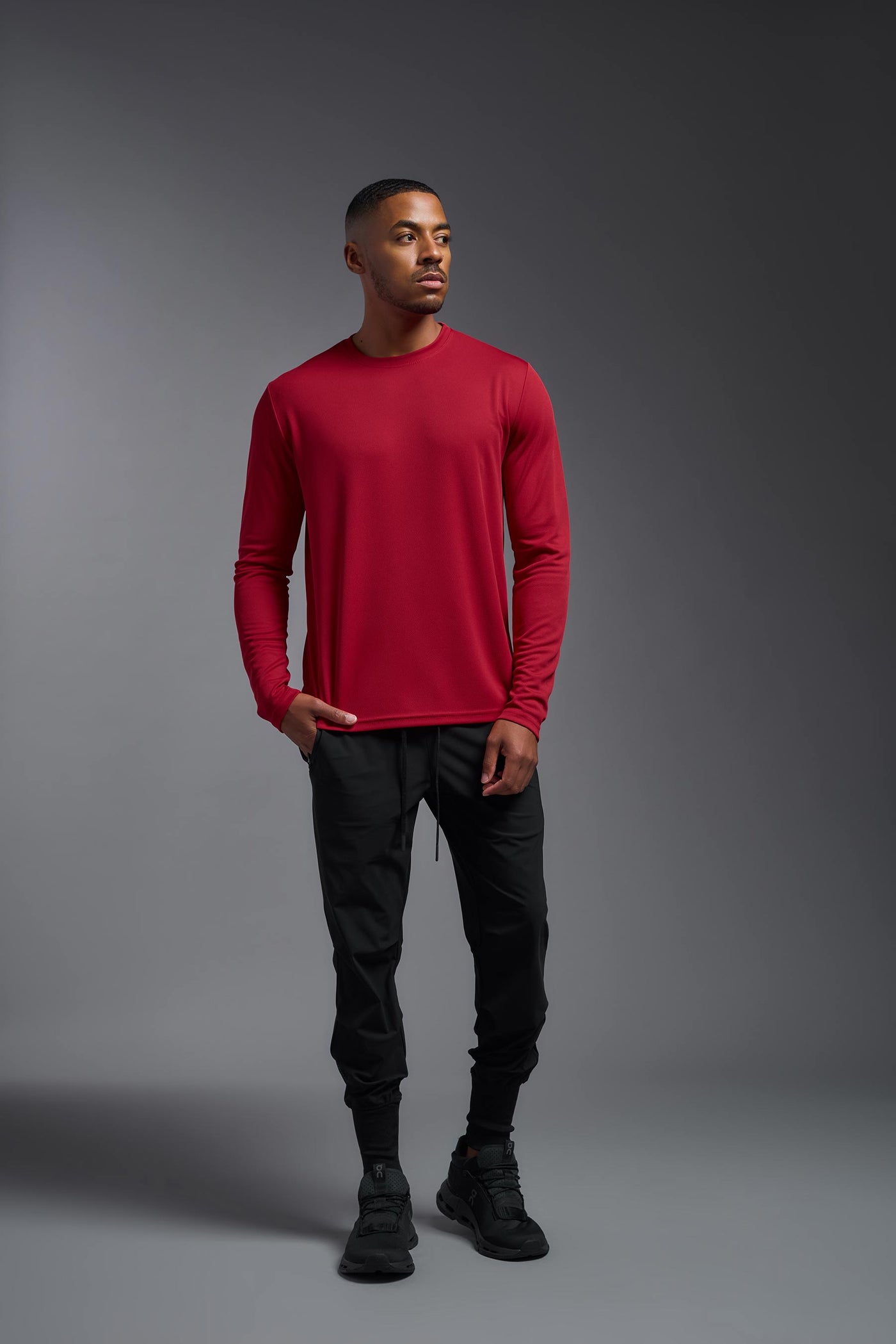 An African American male model with a beard wearing the men's Oxymesh Long Sleeve Tech Tee in the color true red on a gray background, made out of 100% polyester, showing the relaxed fit from a full body front view. This shirt is breathable, quick-drying, moisture-wicking, and made in the USA. #color_true-red