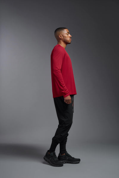 An African American male model with a beard wearing the men's Oxymesh Long Sleeve Tech Tee in the color true red on a gray background, made out of 100% polyester, showing the relaxed fit from a full body side view. This shirt is breathable, quick-drying, moisture-wicking, and made in the USA. #color_true-red