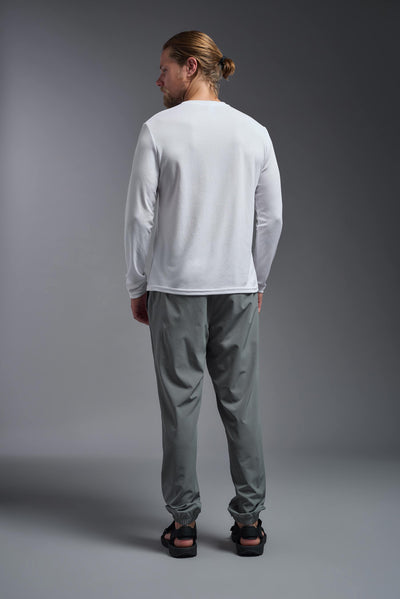 A blonde Caucasian male model with a beard wearing the men's Oxymesh Long Sleeve Tech Tee in the color white on a gray background, made out of 100% polyester, showing the relaxed fit from a full body back view. This shirt is breathable, quick-drying, moisture-wicking, and made in the USA. #color_white