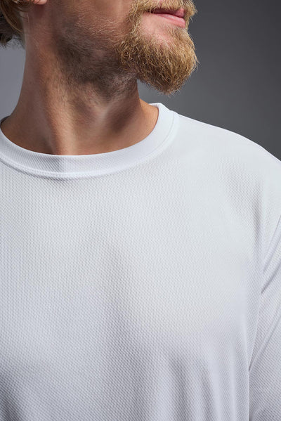 A blonde Caucasian male model with a beard wearing the men's Oxymesh Long Sleeve Tech Tee in the color white on a gray background, made out of 100% polyester, showing the relaxed fit from a closeup collar view. This shirt is breathable, quick-drying, moisture-wicking, and made in the USA. #color_white