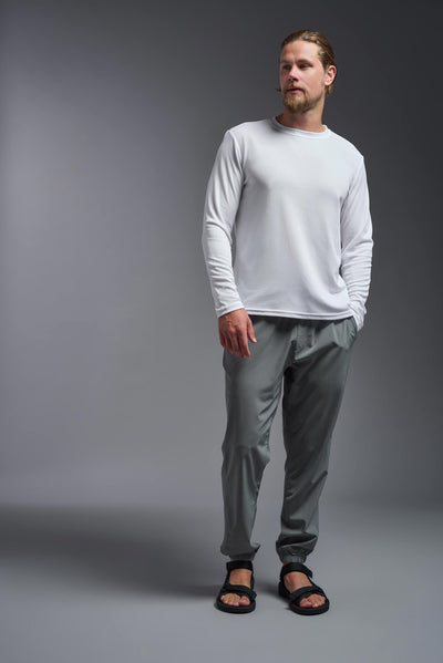 A blonde Caucasian male model with a beard wearing the men's Oxymesh Long Sleeve Tech Tee in the color white on a gray background, made out of 100% polyester, showing the relaxed fit from a full body front view. This shirt is breathable, quick-drying, moisture-wicking, and made in the USA. #color_white