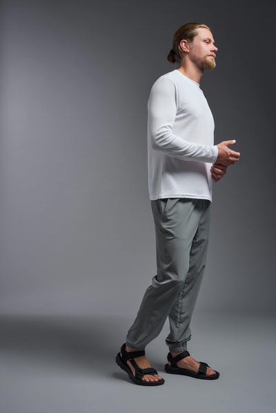 A blonde Caucasian male model with a beard wearing the men's Oxymesh Long Sleeve Tech Tee in the color white on a gray background, made out of 100% polyester, showing the relaxed fit from a full body side view. This shirt is breathable, quick-drying, moisture-wicking, and made in the USA. #color_white