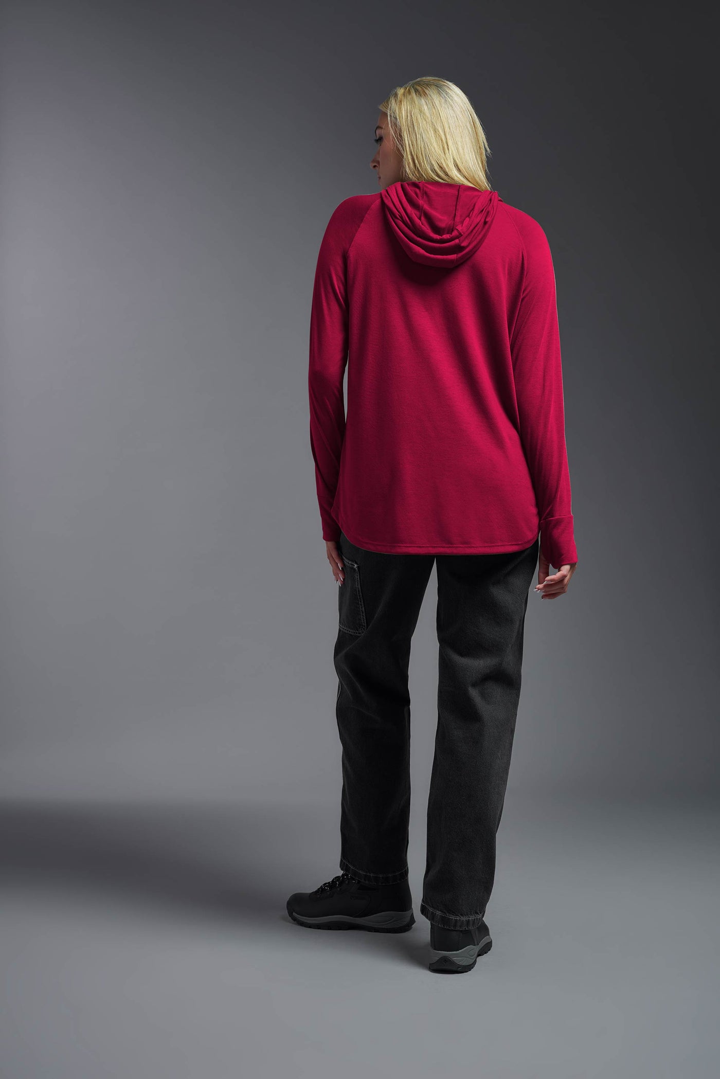 A blonde female model with long straight hair on a gray background, wearing the Women's Siro Curvy Hoodie Shirt in the color scarlet from a full body back view. This hoodie shirt is made in the USA and is quick-drying and moisture-wicking. #color_scarlet