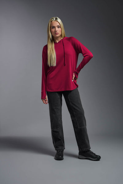 A blonde female model with long straight hair on a gray background, wearing the Women's Siro Curvy Hoodie Shirt in the color scarlet from a full body front view. This hoodie shirt is made in the USA and is quick-drying and moisture-wicking. #color_scarlet