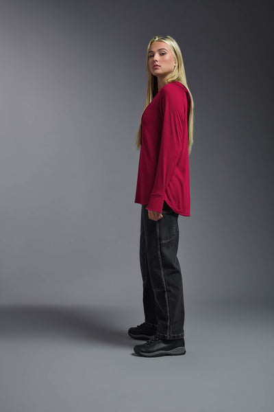 A blonde female model with long straight hair on a gray background, wearing the Women's Siro Curvy Hoodie Shirt in the color scarlet from a full body side view. This hoodie shirt is made in the USA and is quick-drying and moisture-wicking. #color_scarlet