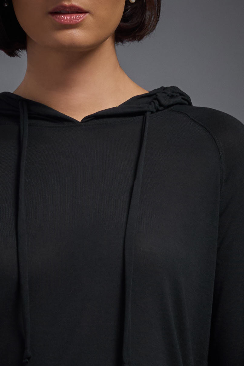 A female model with short brown hair on a gray background, wearing the Women's Siro Curvy Hoodie Shirt in the color black from a front collar detail view. This hoodie shirt is made in the USA and is quick-drying and moisture-wicking. #color_black