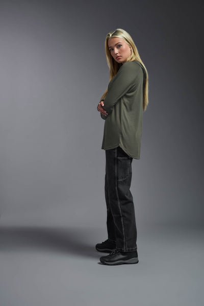 A blonde female model with long straight hair on a gray background, wearing the Women's Siro Curvy Hoodie Shirt in the color olive green from a full body side view. This hoodie shirt is made in the USA and is quick-drying and moisture-wicking. #color_olive