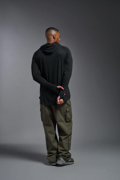 An African American, male model with a beard wearing the men's Siro Curvy Hoodie Shirt in the color black back, made out of 100% polyester, showing the relaxed fit from a back view. This shirt features a soft cotton feel, quick-dries, wicks moisture and is made in the USA. #color_black