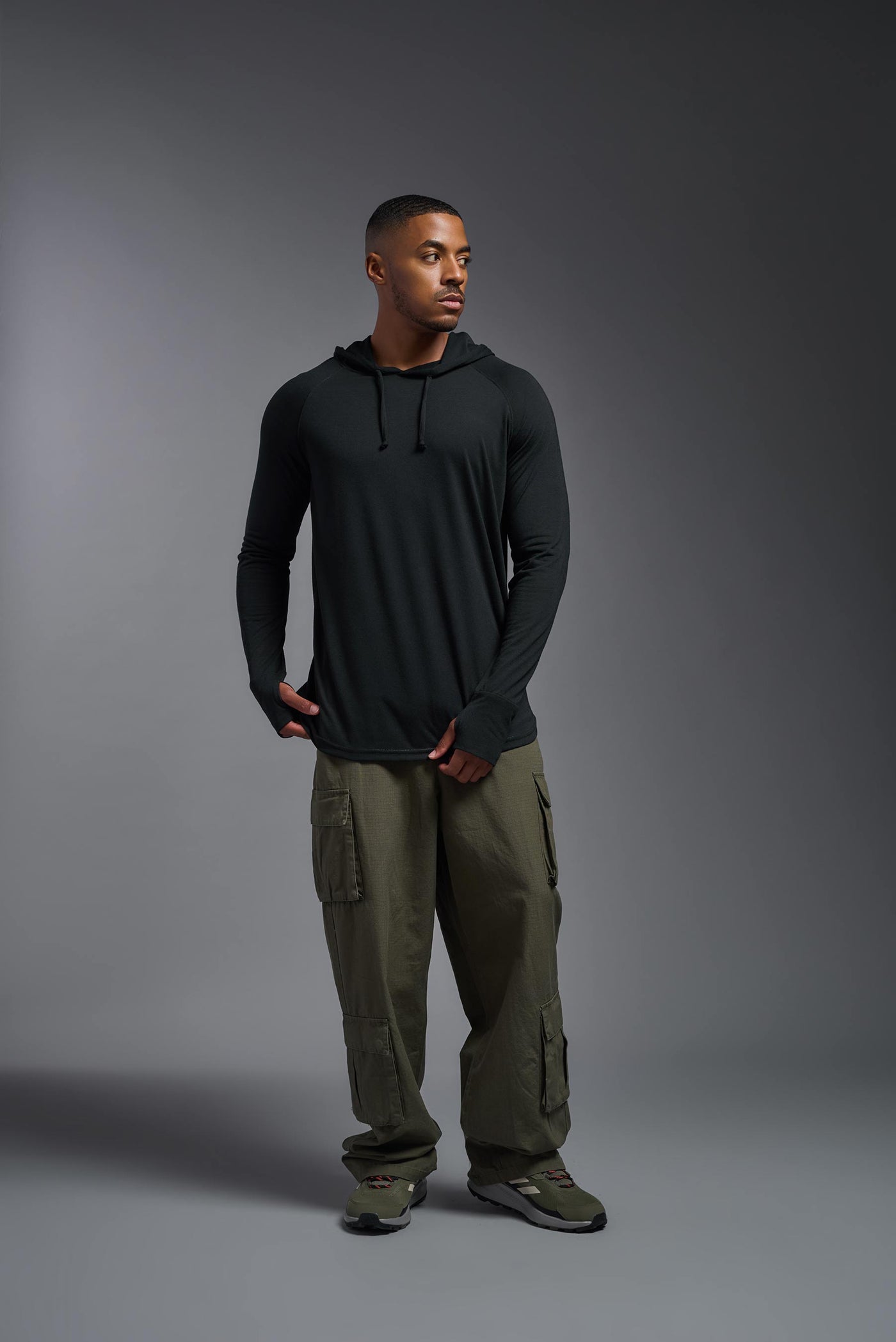 An African American, male model with a beard wearing the men's Siro Curvy Hoodie Shirt in the color black, made out of 100% polyester, showing the relaxed fit from a front view. This shirt features a soft cotton feel, quick-dries, wicks moisture and is made in the USA. #color_black