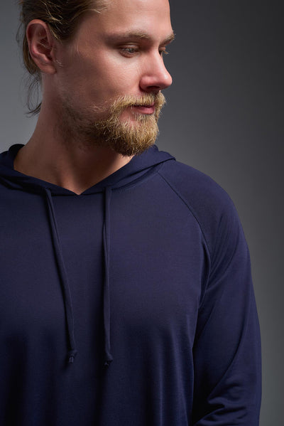A blonde male model with a beard wearing the men's Siro Curvy Hoodie Shirt in the color navy, made out of 100% polyester, showing the relaxed fit from a closeup collar view. This hoodie shirt features a soft cotton feel, quick-dries, wicks moisture and is made in the USA. #color_navy