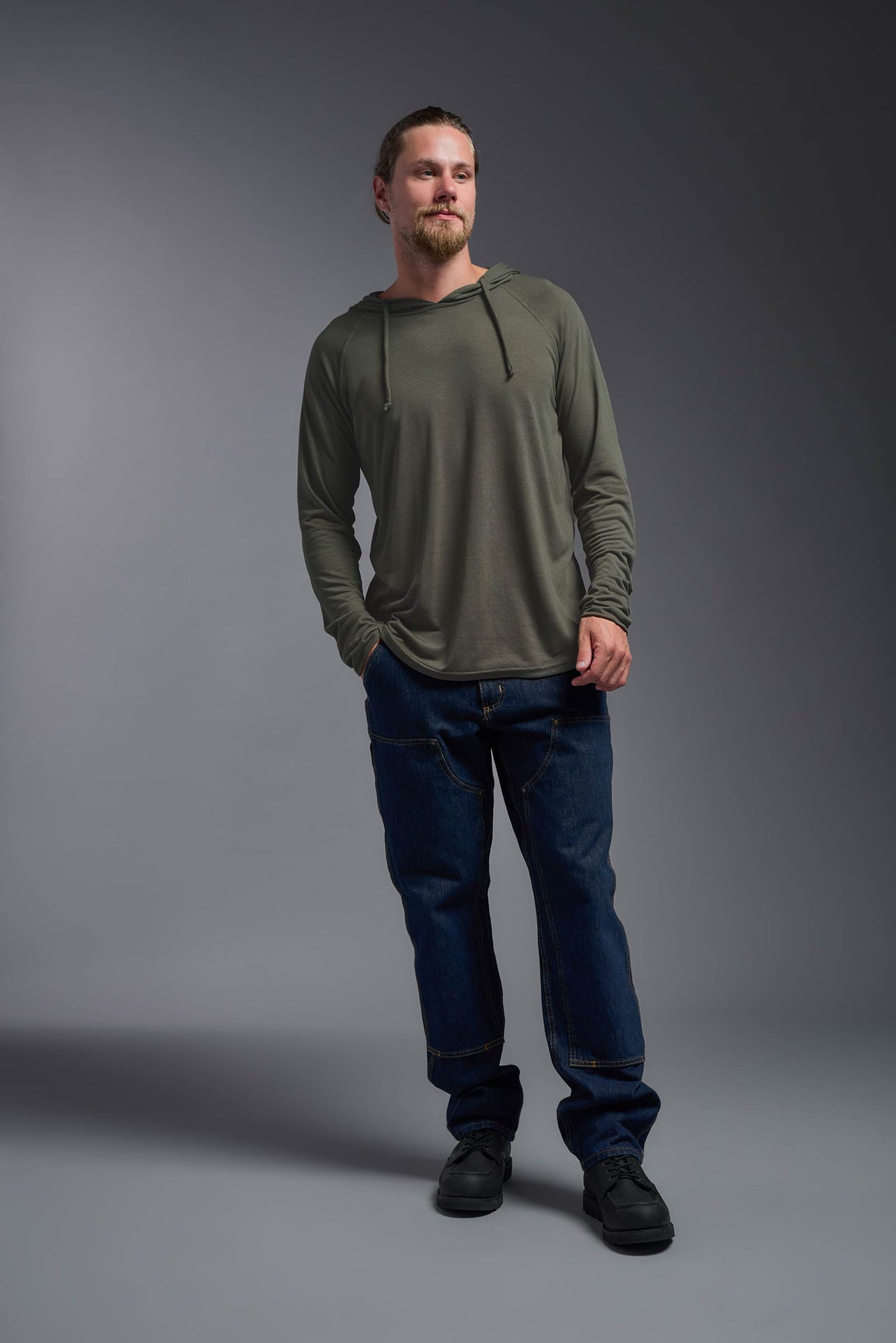 A blonde male model with a beard wearing the men's Siro Curvy Hoodie Shirt in the color olive, made out of 100% polyester, showing the relaxed fit from a front view. This hoodie shirt features a soft cotton feel, quick-dries, wicks moisture and is made in the USA. #color_olive
