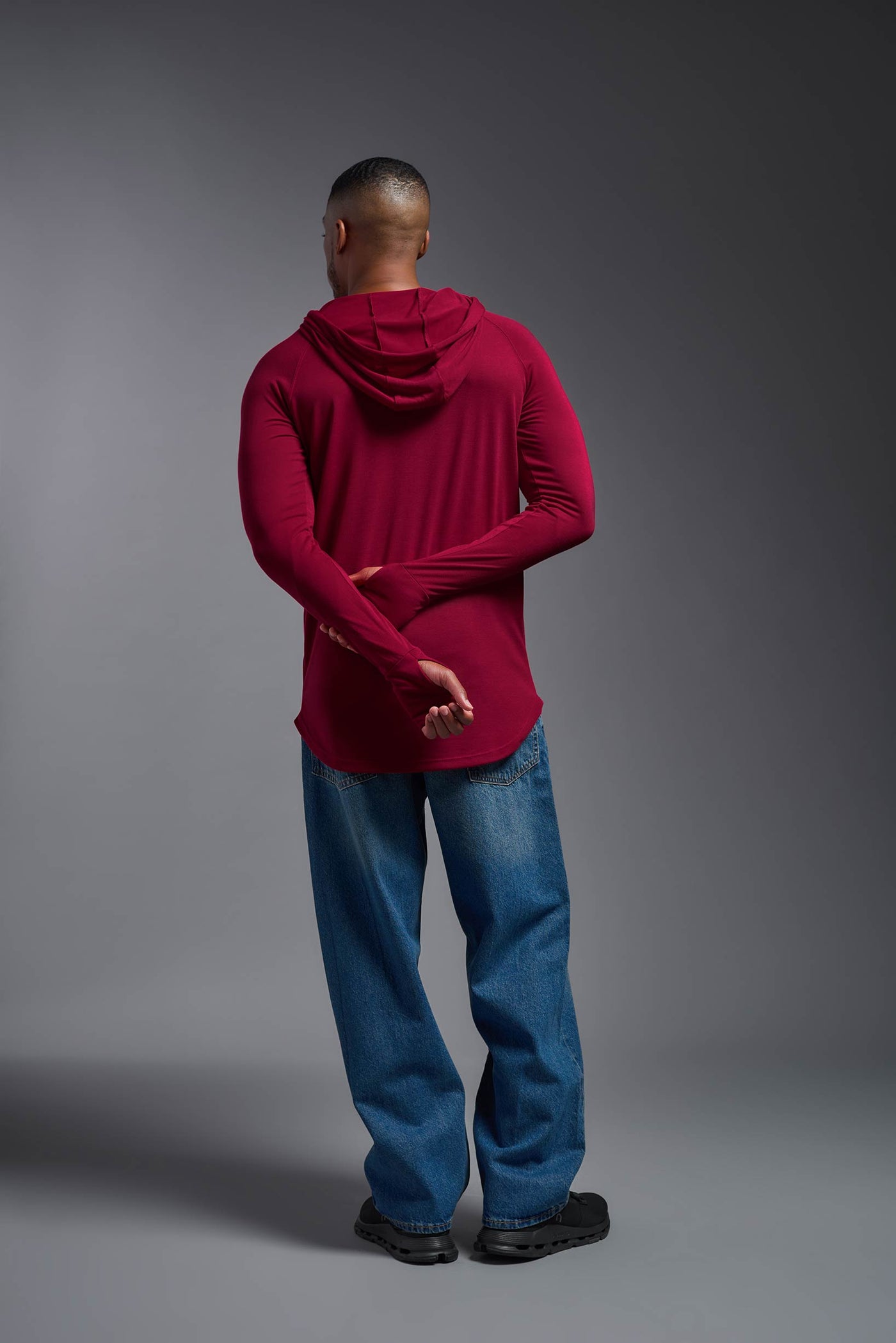 An African American, male model with a beard wearing the men's Siro Curvy Hoodie Shirt in the color scarlet, made out of 100% polyester, showing the relaxed fit from a back view. This shirt features a soft cotton feel, quick-dries, wicks moisture and is made in the USA. #color_scarlet