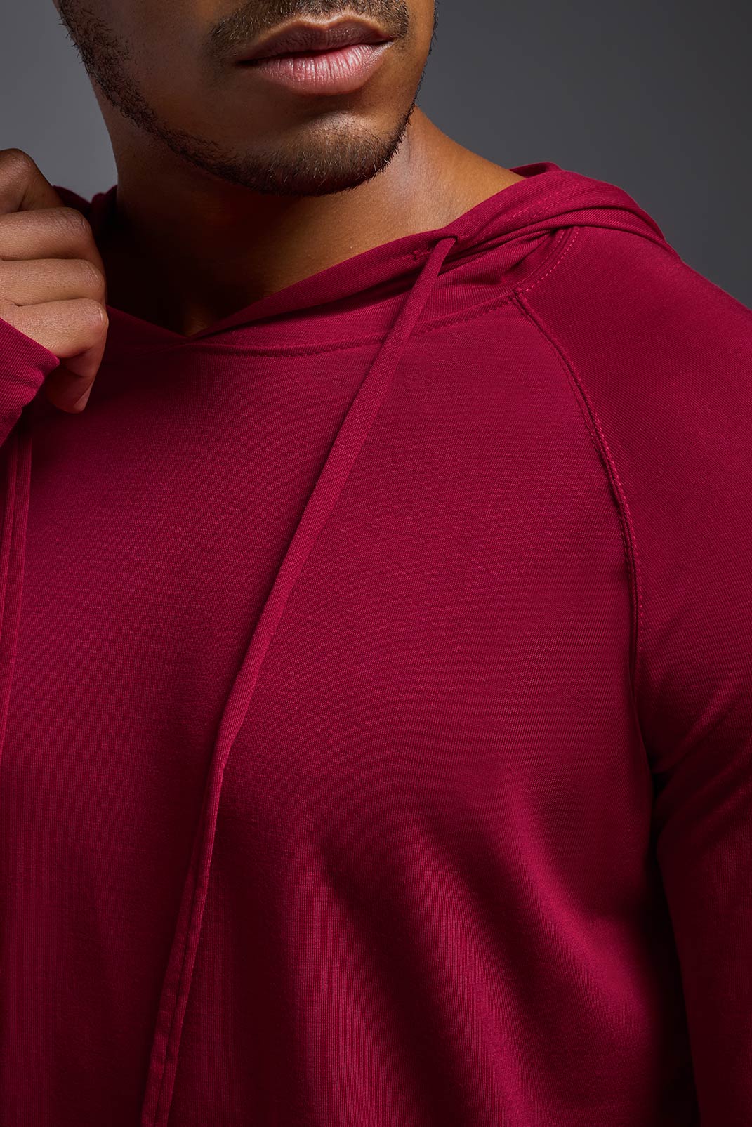 An African American, male model with a beard wearing the men's Siro Curvy Hoodie Shirt in the color scarlet, made out of 100% polyester, showing the relaxed fit from a front collar detail view. This shirt features a soft cotton feel, quick-dries, wicks moisture and is made in the USA. #color_scarlet