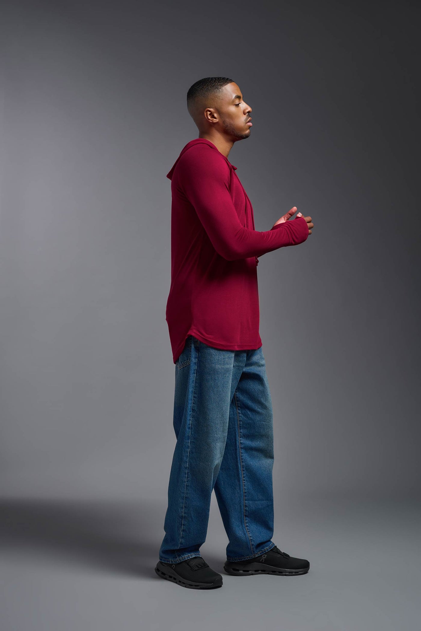 An African American, male model with a beard wearing the men's Siro Curvy Hoodie Shirt in the color scarlet, made out of 100% polyester, showing the relaxed fit from a side view. This shirt features a soft cotton feel, quick-dries, wicks moisture and is made in the USA. #color_scarlet