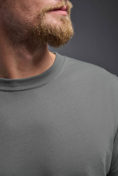 A male caucasian model with a beard wearing the men's DuroSoft Outdoor Tee in the color army gray on a gray background, made out of 100% filament polyester that feels like soft cotton, showing the modern fit from a front collar closeup view. This shirt is anti-snagging, quick-drying and moisture-wicking and is made in the USA. #color_army-gray