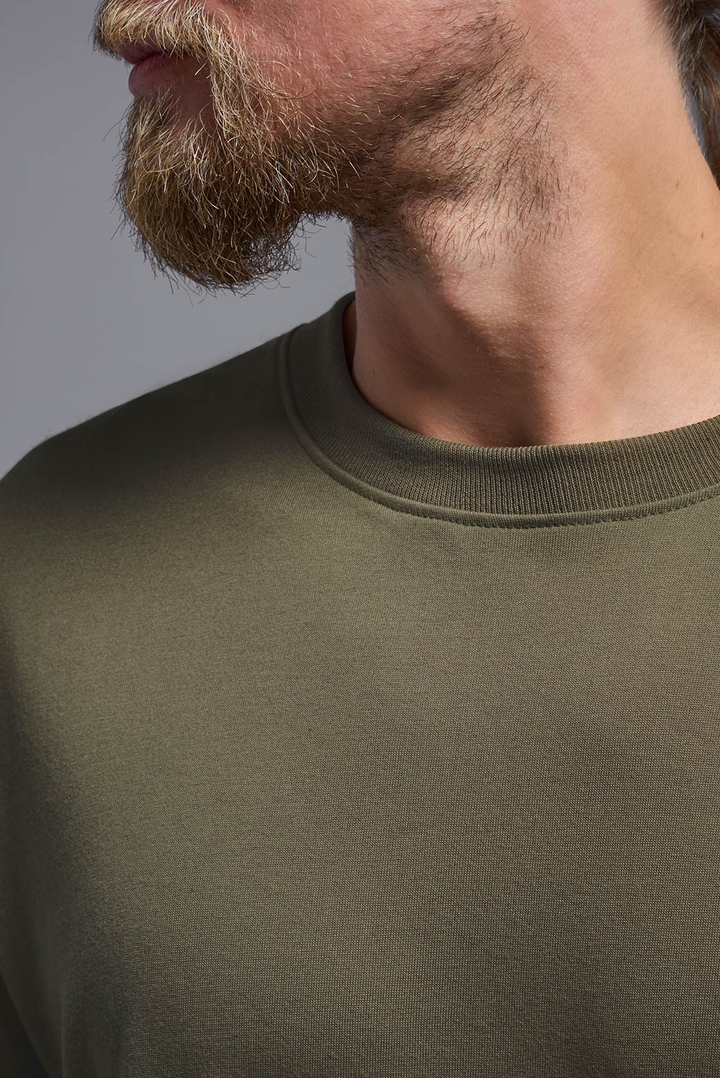 A male caucasian model with a beard wearing the men's DuroSoft Outdoor Tee in the color desert on a gray background, made out of 100% filament polyester that feels like soft cotton, showing the modern fit from a front collar closeup view. This shirt is anti-snagging, quick-drying and moisture-wicking and is made in the USA. #color_tan-499