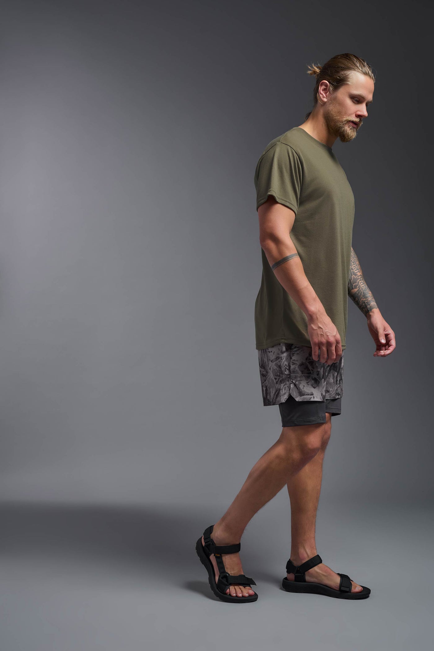 A male caucasian model with a beard wearing the men's DuroSoft Outdoor Tee in the color tan 499 on a gray background, made out of 100% filament polyester that feels like soft cotton, showing the modern fit from a side view. This shirt is anti-snagging, quick-drying and moisture-wicking and is made in the USA. #color_tan-499
