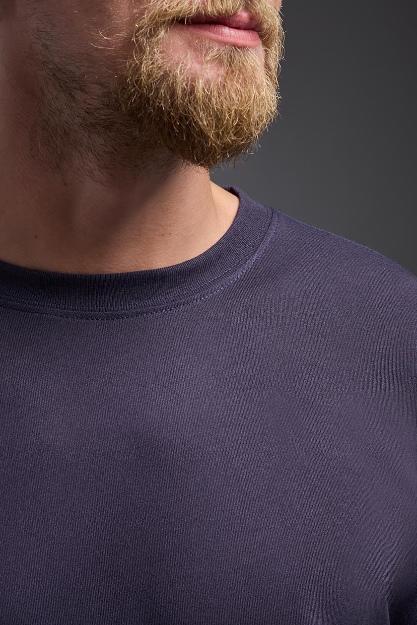 A male caucasian model with a beard wearing the men's DuroSoft Outdoor Tee in the color army blue on a gray background, made out of 100% filament polyester that feels like soft cotton, showing the modern fit from a close-up collar view. This shirt is anti-snagging, quick-drying and moisture-wicking and is made in the USA. #color_army-blue