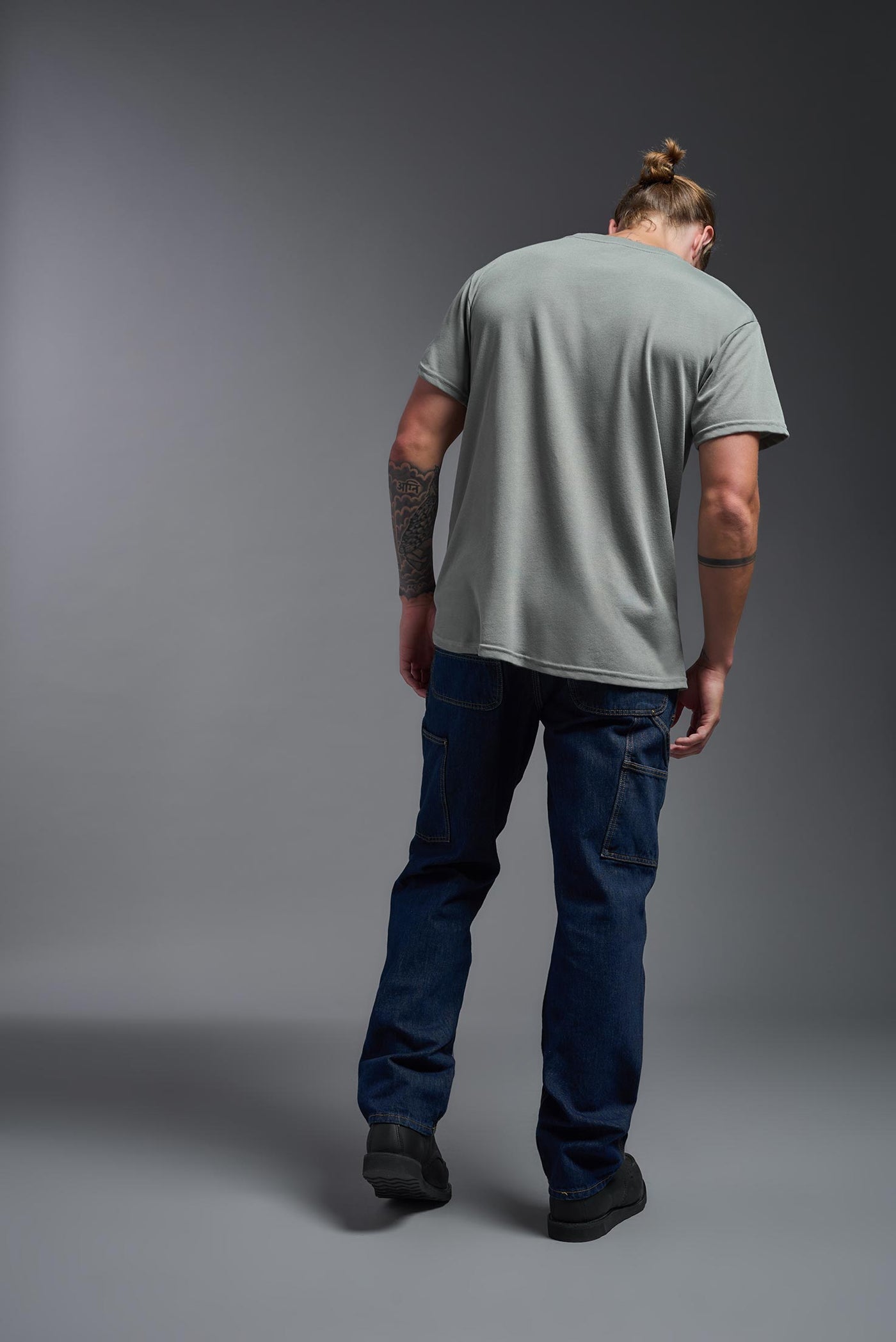 A male caucasian model with a beard wearing the men's DuroSoft Outdoor Tee in the color army gray on a gray background, made out of 100% filament polyester that feels like soft cotton, showing the modern fit from a back view. This shirt is anti-snagging, quick-drying and moisture-wicking and is made in the USA. #color_army-gray