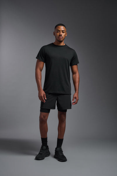 A male African American model with a beard wearing the men's DuroSoft Outdoor Tee in the color black on a gray background, made out of 100% filament polyester that feels like soft cotton, showing the modern fit from a front view. This shirt is anti-snagging, quick-drying and moisture-wicking and is made in the USA. #color_black