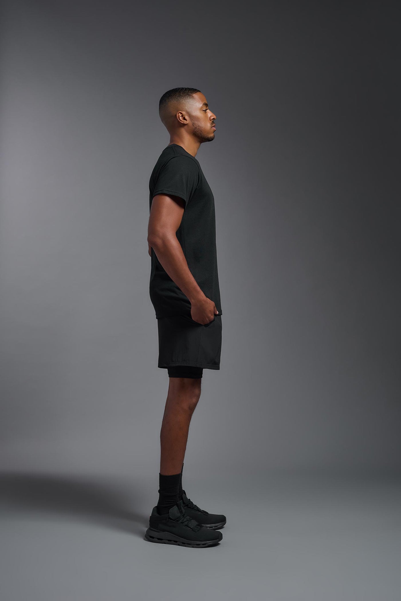A male African American model with a beard wearing the men's DuroSoft Outdoor Tee in the color black on a gray background, made out of 100% filament polyester that feels like soft cotton, showing the modern fit from a side view. This shirt is anti-snagging, quick-drying and moisture-wicking and is made in the USA. #color_black