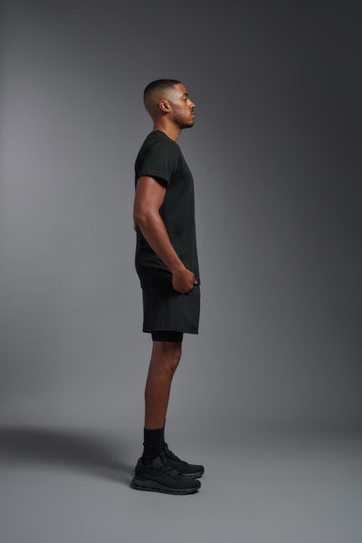 A male African American model with a beard wearing the men's DuroSoft Outdoor Tee in the color black on a gray background, made out of 100% filament polyester that feels like soft cotton, showing the modern fit from a side view. This shirt is anti-snagging, quick-drying and moisture-wicking and is made in the USA. #color_black