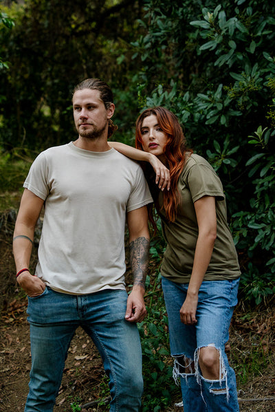 A male caucasian model with a beard and a woman with red hear wearing the DuroSoft Outdoor Tee in the color desert and tan 499 while standing in the forest. This shirt is made out of 100% filament polyester that feels like soft cotton,and is anti-snagging, quick-drying and moisture-wicking and is made in the USA. #color_desert