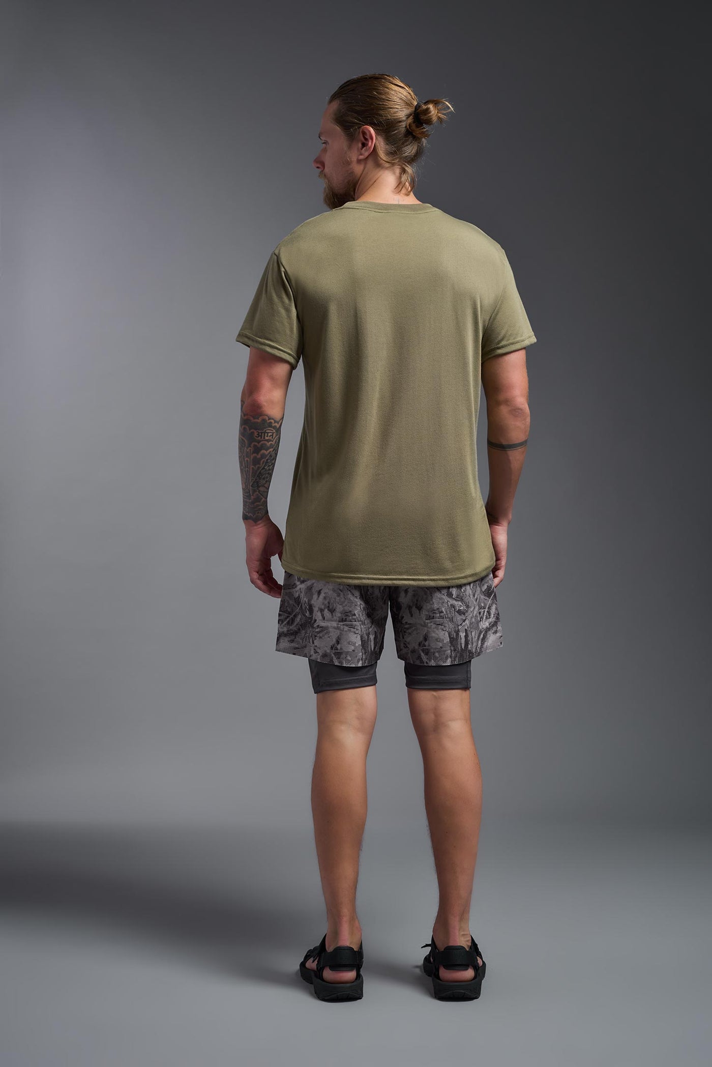 A male caucasian model with a beard wearing the men's DuroSoft Outdoor Tee in the color tan 499 on a gray background, made out of 100% filament polyester that feels like soft cotton, showing the modern fit from a back view. This shirt is anti-snagging, quick-drying and moisture-wicking and is made in the USA. #color_tan-499