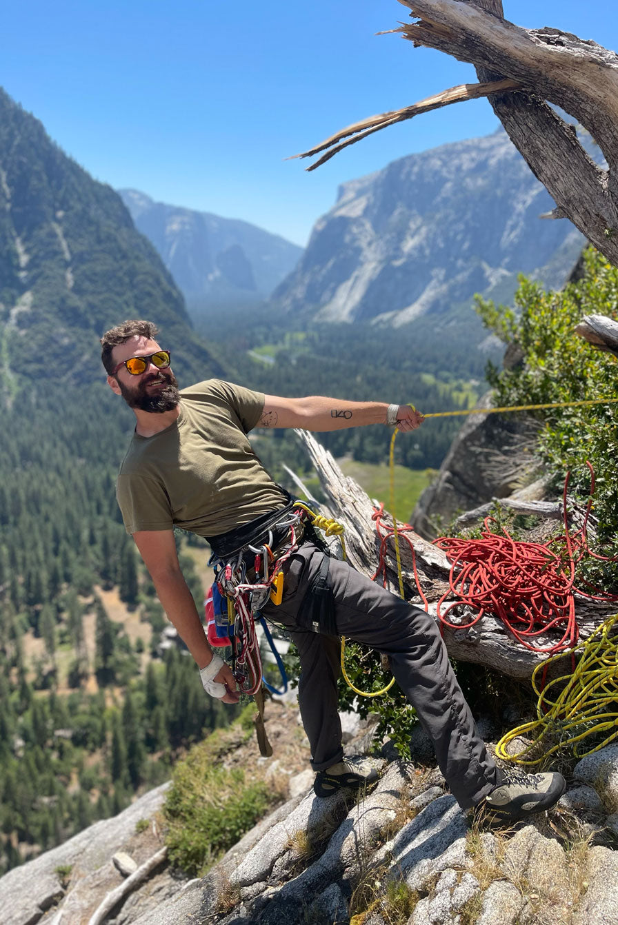 A male caucasian model with a beard wearing the men's DuroSoft Outdoor Tee in the color tan 499  holding a rock climbing rope in Yosemite. This shirt is made out of 100% filament polyester that feels like soft cotton, features a modern fit. This shirt is anti-snagging, quick-drying and moisture-wicking and is made in the USA. #color_tan-499