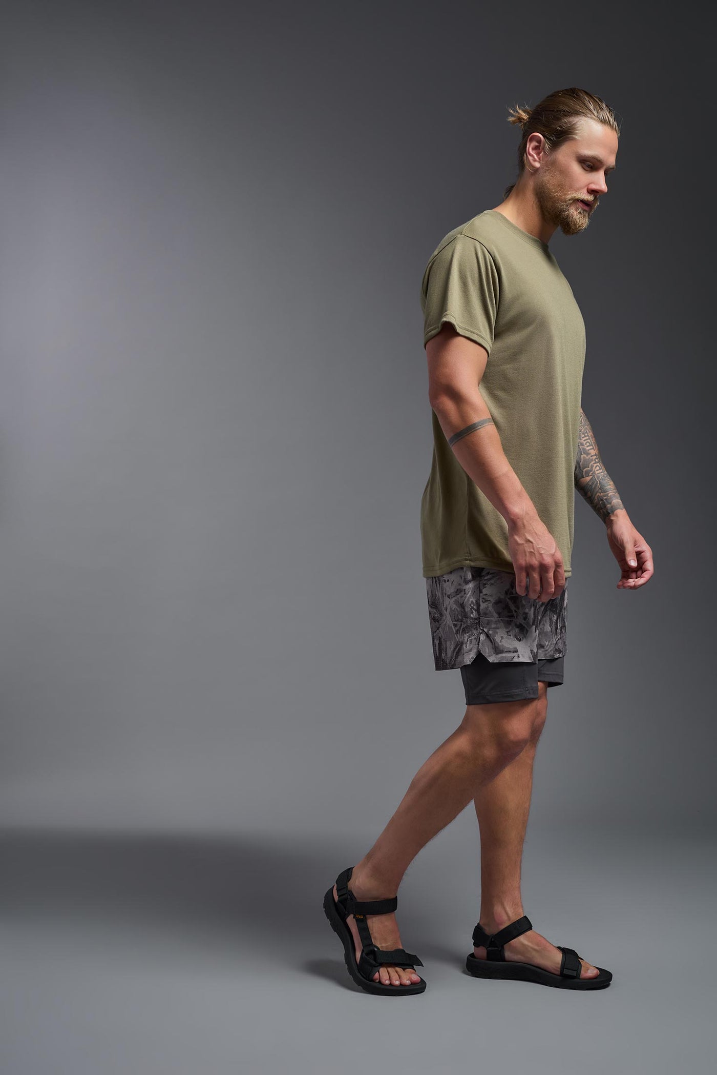 A male caucasian model with a beard wearing the men's DuroSoft Outdoor Tee in the color tan 499 on a gray background, made out of 100% filament polyester that feels like soft cotton, showing the modern fit from a side view. This shirt is anti-snagging, quick-drying and moisture-wicking and is made in the USA. #color_tan-499