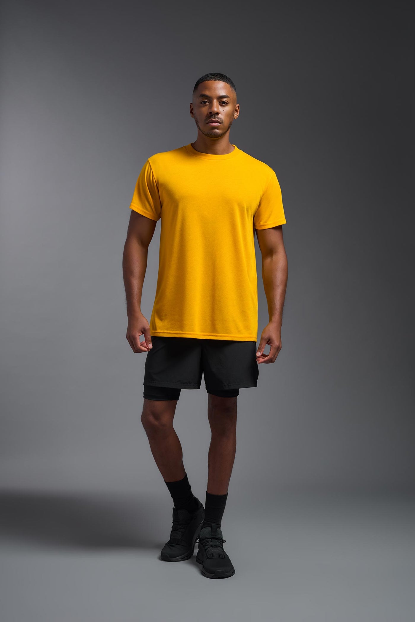 A male african-american model  wearing the men's DuroSoft Outdoor Tee in the color yellow on a gray background, made out of 100% filament polyester that feels like soft cotton, showing the modern fit from a front view. This shirt is anti-snagging, quick-drying and moisture-wicking and is made in the USA. #color_yellow