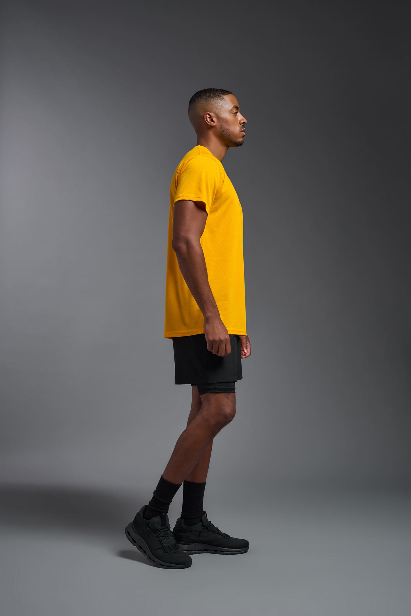A male african-american model wearing the men's DuroSoft Outdoor Tee in the color yellow on a gray background, made out of 100% filament polyester that feels like soft cotton, showing the modern fit from a side view. This shirt is anti-snagging, quick-drying and moisture-wicking and is made in the USA. #color_yellow